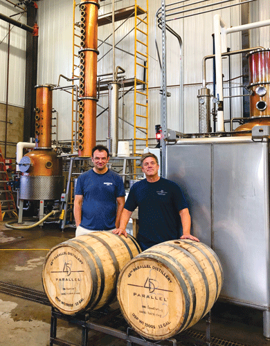 Bob McKenzie and Scott Davis pose with two barrels of scotch. The German-made copper stills are in the background. Photo by Josie Werni.