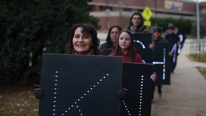 Kim Blaeser leads participants at the first #LanguageBack workshop holding lighted signs that will to spell out Neka:mwan, the Mohican word for song.