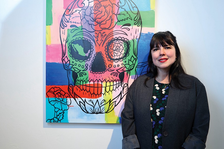 Artist Issis Macias standing in front of her collaboration piece with Artist Rodrigo Carapia, featured at Common Wealth Development and LOUD’s Día de Muertos Gallery Night. Photo by Martin Jenich