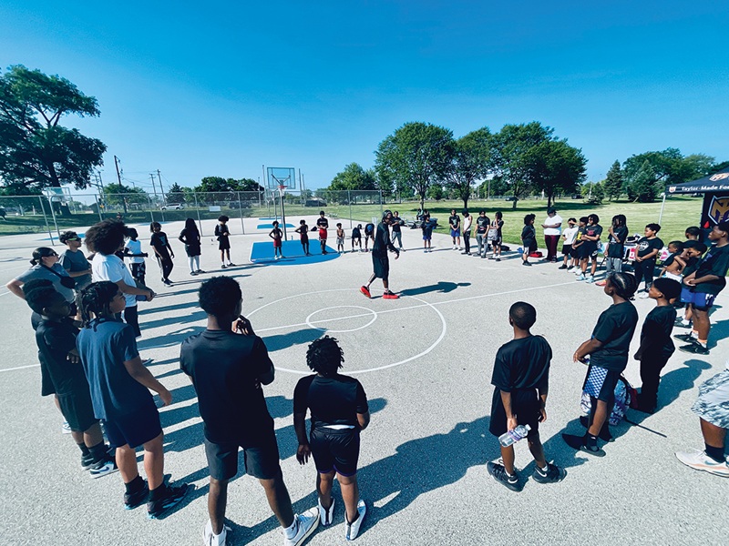 Taylor gathers his young players in a circle on the McGovern Park courts to begin their time together. Taylor gathers his young players in a circle on the McGovern Park courts to begin their time together.