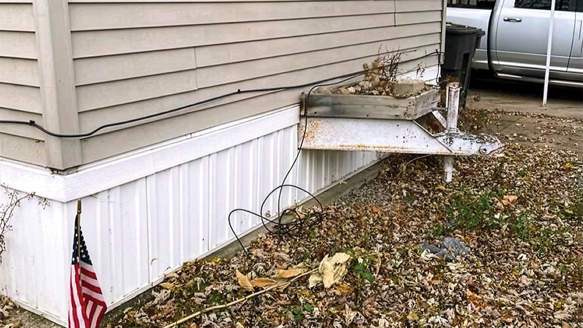 The rusted triangular frame, which once supported the hitch coupler for towing the manufactured home, now serves as a stand for a decorative planter. Credit: Erin Gaede.
